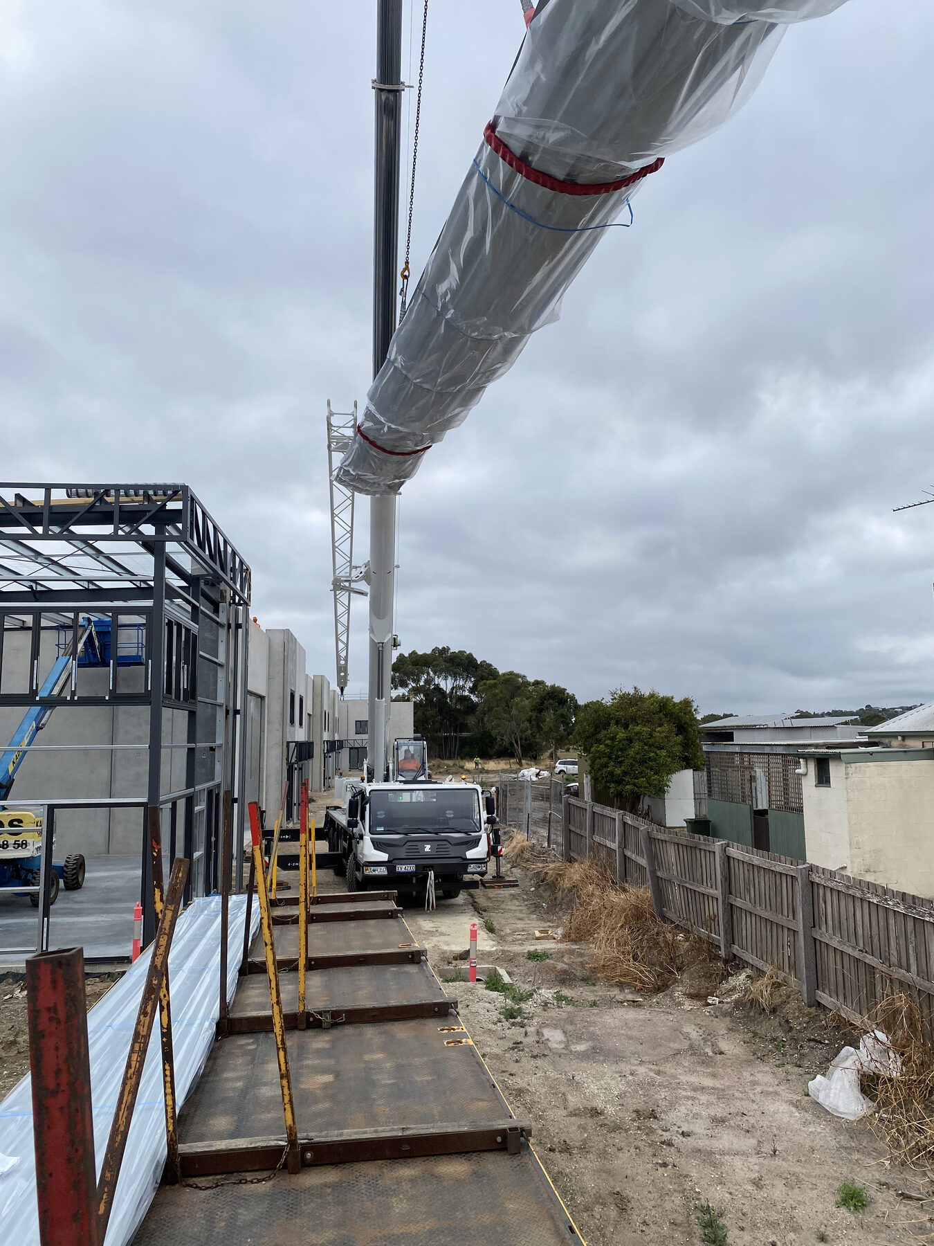 Crane lifting wrapped ductwork onto a steel-framed building